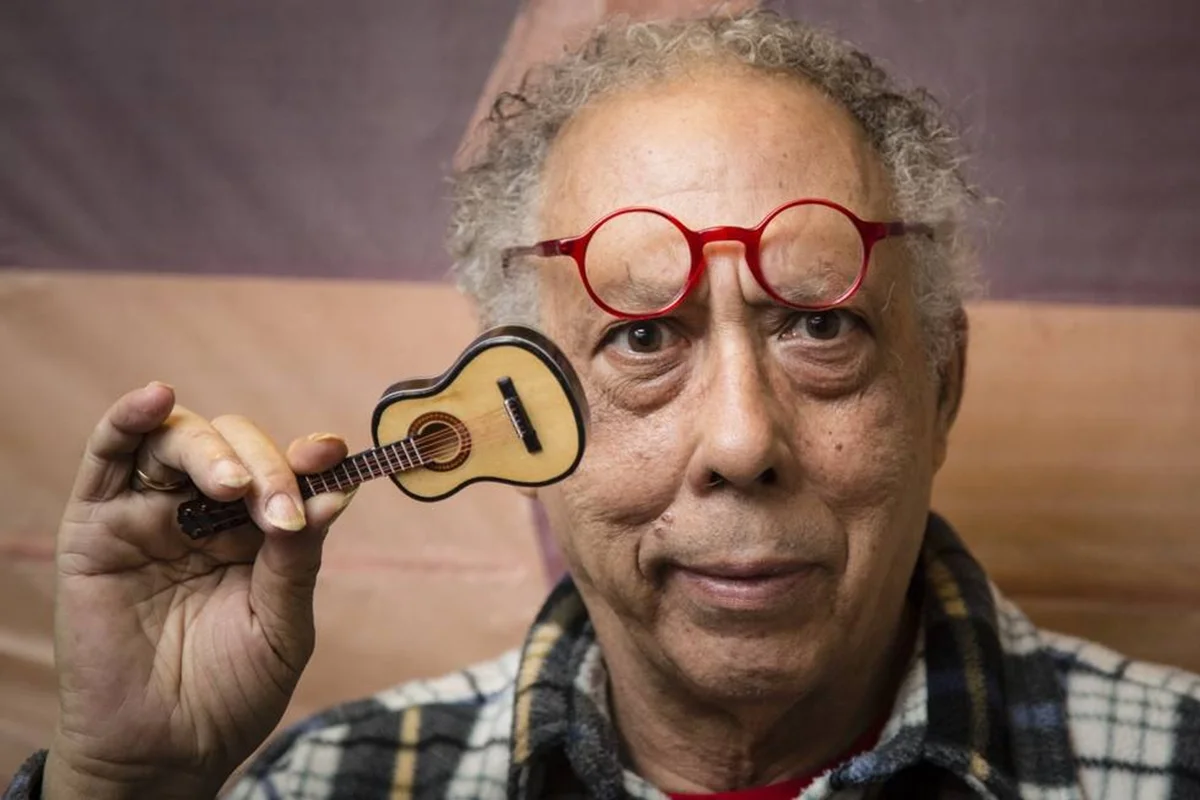 Jards Macalé segurando um cavaquinho em frente ao rosto